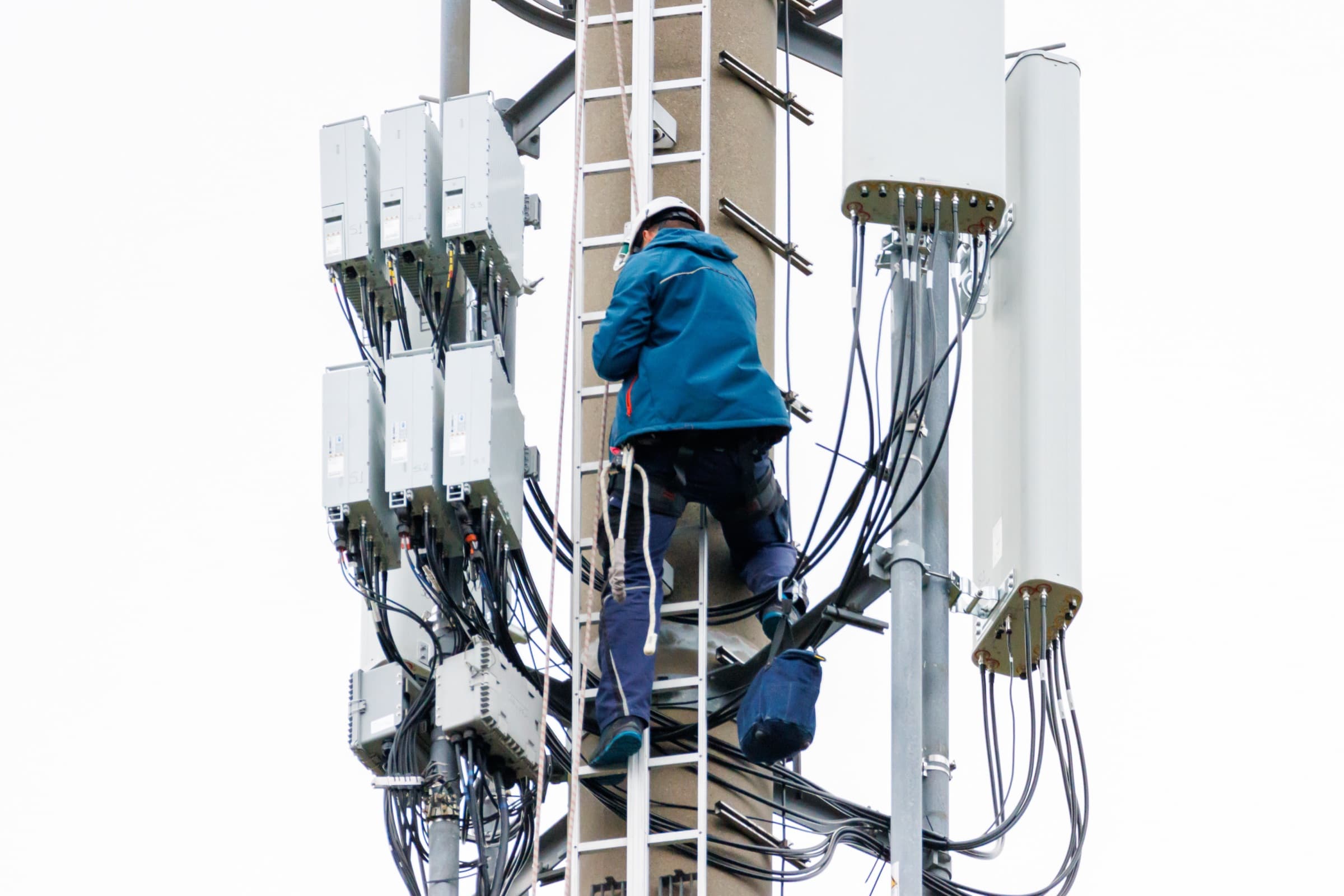 An engineer climbing a mast, working on the radio units of a cell site.